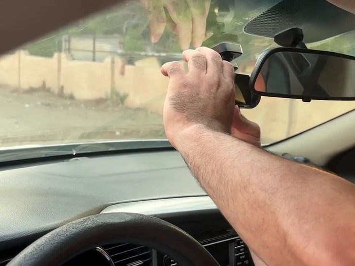 A hand pressing the LYNX Guardian 360 onto its windshield mount behind the rear-view mirror of a parked car.