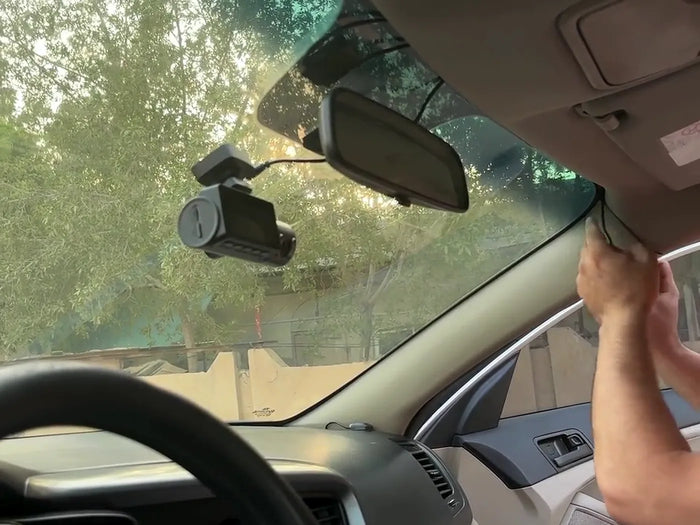A hand tucking the dash cam cable behind the A-pillar trim of a parked car.